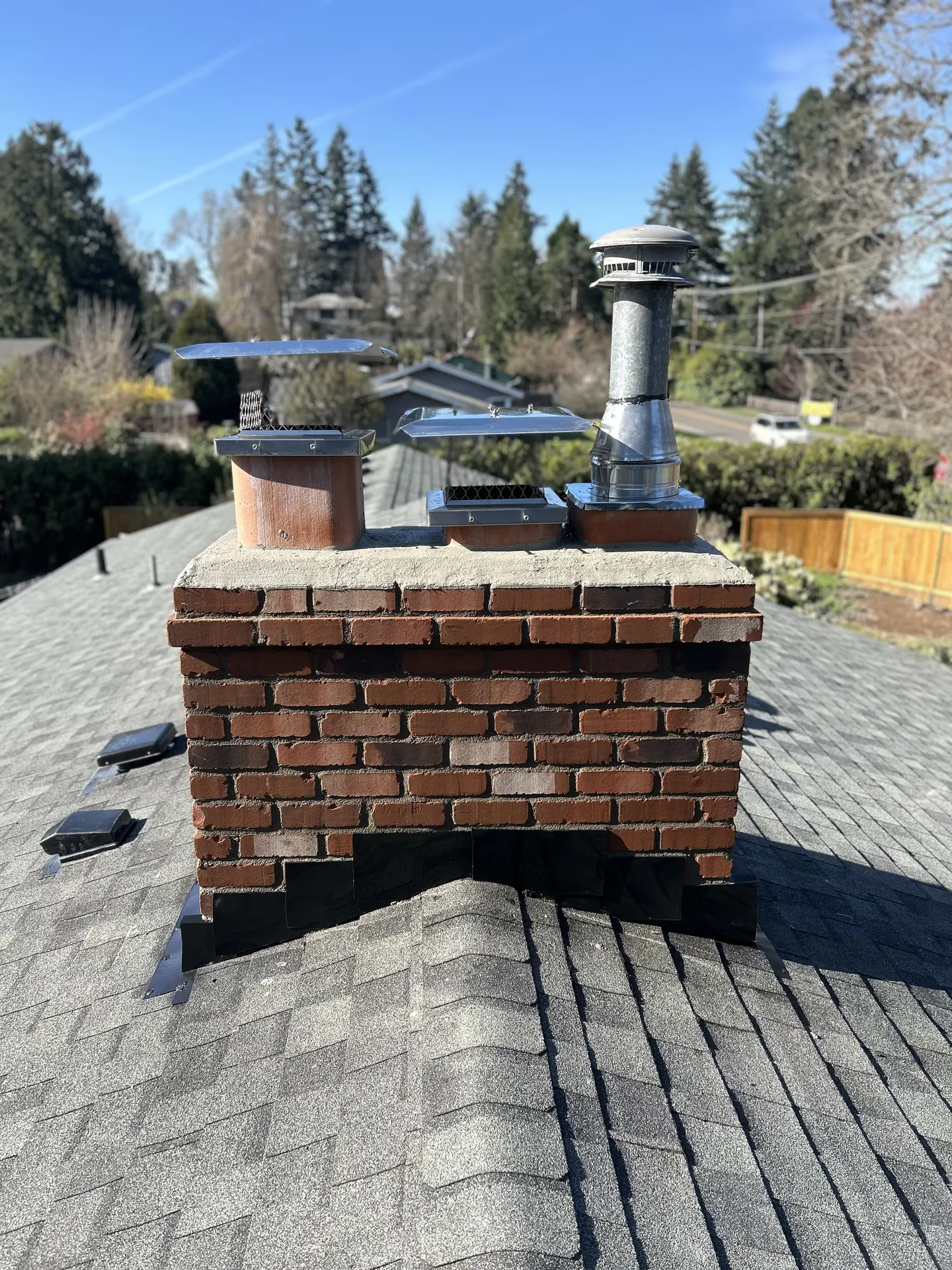 A brick chimney crown and flue caps inspected by a First Rate Chimney tech on a Portland metro rooftop