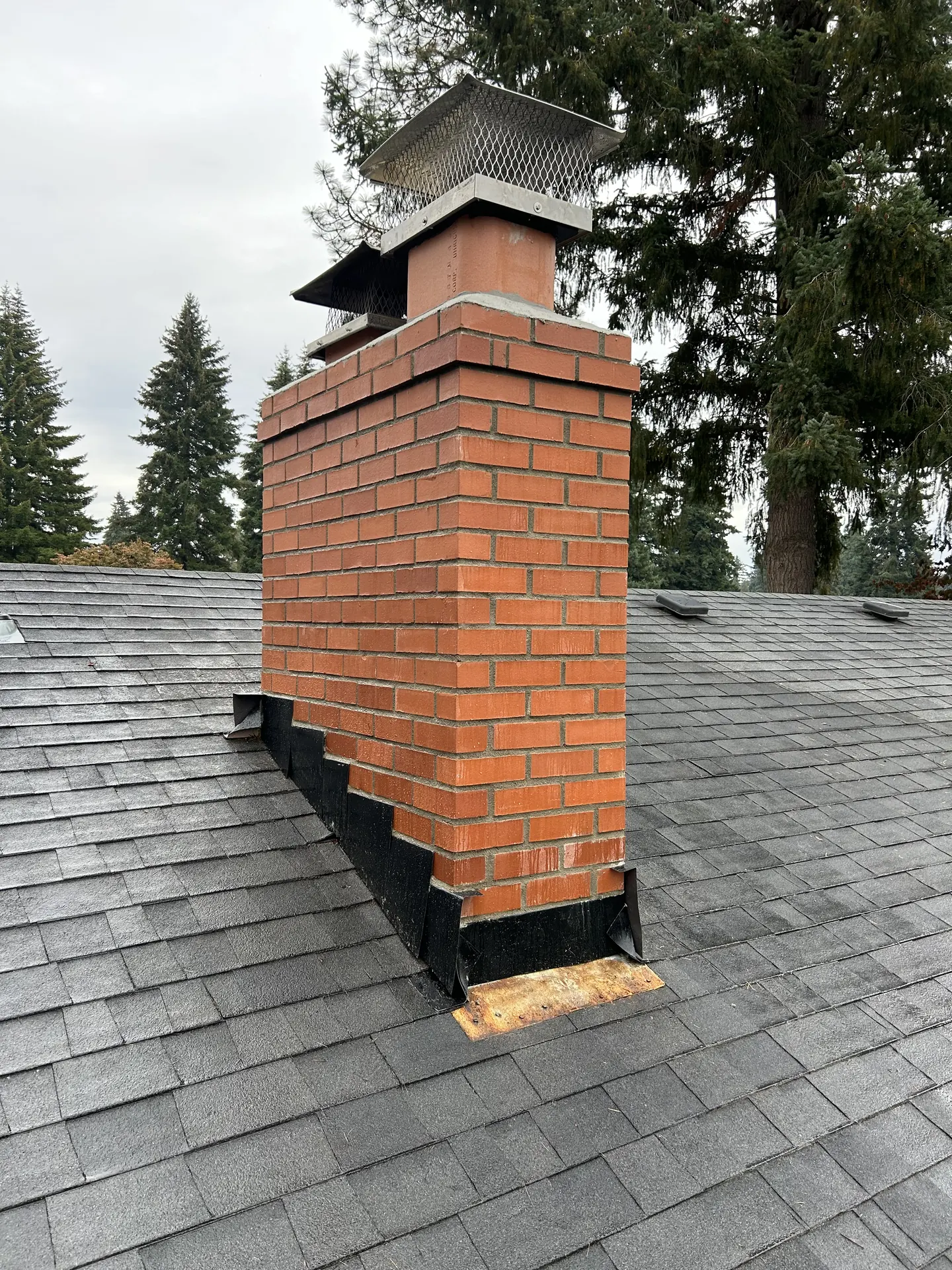 A tall orange brick chimney rebuilt by First Rate Chimney, framed by evergreens