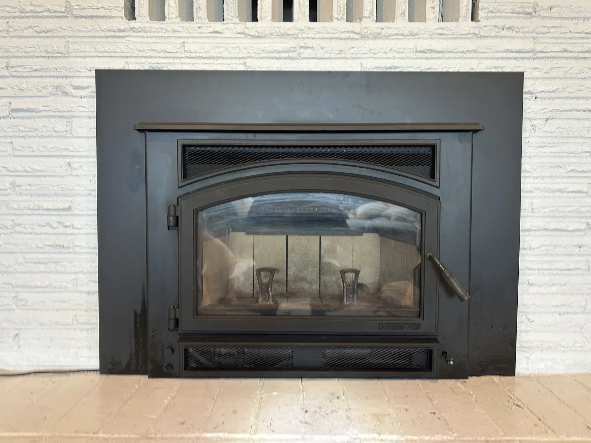 A black wood stove insert installed by First Rate Chimney in a white brick fireplace